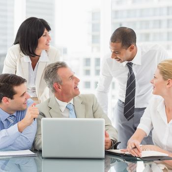 Happy business team gathered around laptop chatting in the office