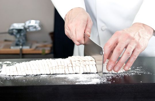 Close-up of a Chef cutting fresh noodles with a pasta rolling machine in the background.