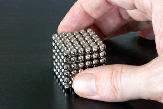 Close-up of a hand pickinf up a cube composed of magnetic balls.