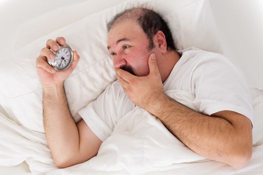Man suffering from insomnia trying to sleep checking the time on his alarm clock in desperation as he realises he will not wake up in time for work if he sleeps now