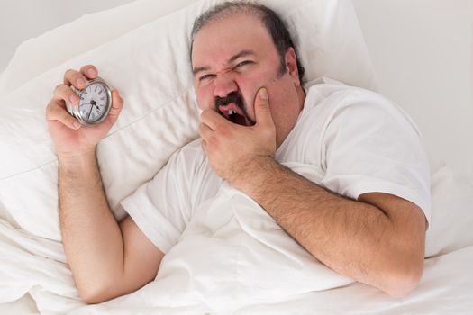 Man suffering from insomnia lying in bed clutching his alarm clock as he checks the time and wonders if he will wake up in the morning for work if he goes to sleep now