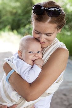 Young Caucasian woman and her baby son in sling outdoors