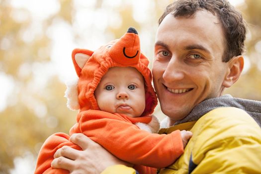 Young Caucasian man and his little son in fox costume in autumn park