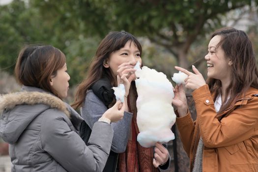 Happy young Asian woman eating cotton candy with her friends in outdoor.