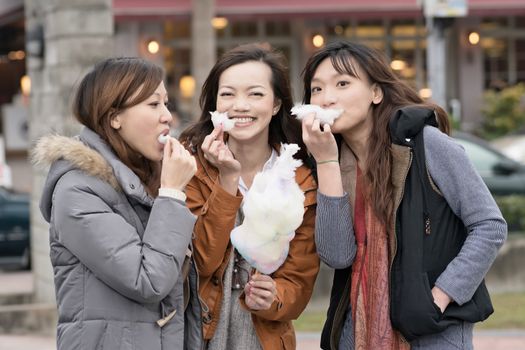 Happy young Asian woman eating cotton candy with her friends in outdoor.