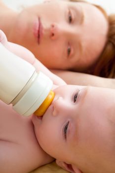 Bond little baby with blue eyes drinking bottle milk with her mother