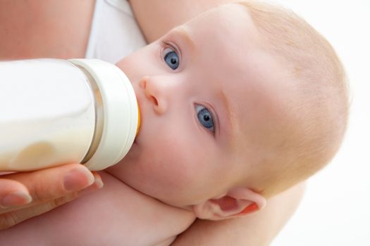Bond little baby with blue eyes drinking bottle milk in mother arms