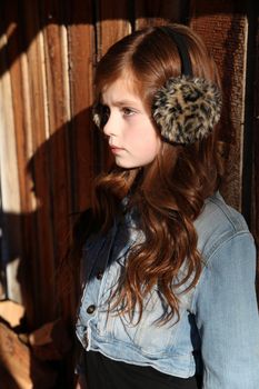 Red haired girl wearing earmuffs against wooden background