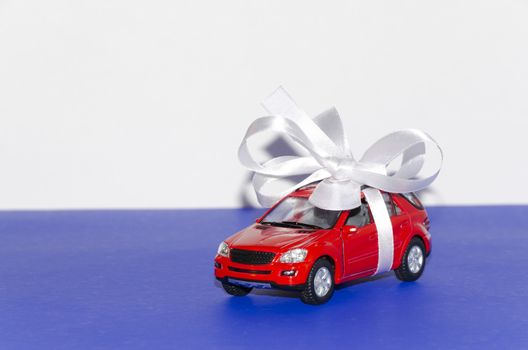 Red car, tied with white ribbon on a blue desktop on a white background