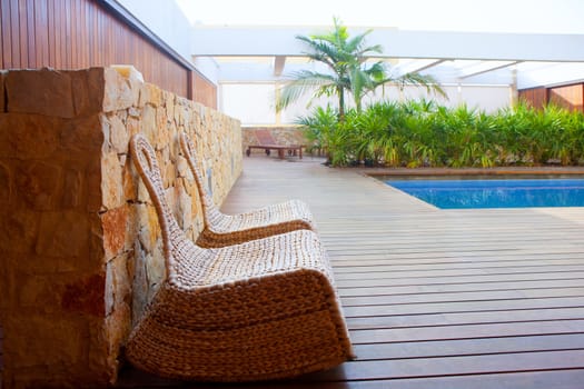 Teak wood modern house outdoor with swing chairs and palm trees pool