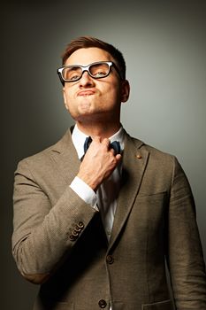 Confident nerd in eyeglasses adjusting his bow-tie against grey background