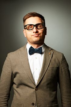 Confident nerd in eyeglasses and bow tie against grey background