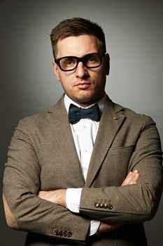 Confident nerd in eyeglasses and bow tie against grey background