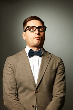 Confident nerd in eyeglasses and bow tie against grey background