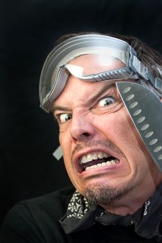 Close-up of a crazy man wearing goggles with a knife loking afraid.