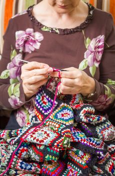 Hands of senior woman knitting a vintage wool quilt with colorful patches