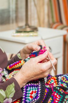 Hands of senior woman knitting a vintage wool quilt with colorful patches