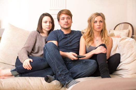 Three fascinated young teenagers sitting watching television glued to the screen with serious anticipation as they enjoy an evening of entertainment together