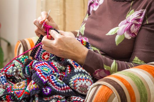 Hands of senior woman knitting a vintage wool quilt with colorful patches