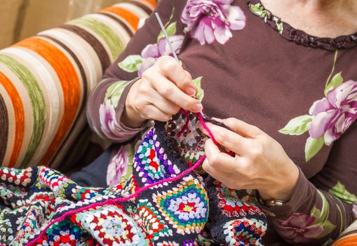 Hands of senior woman knitting a vintage wool quilt with colorful patches