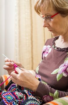 Portrait of senior woman knitting a vintage wool quilt with colorful patches