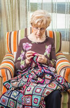 Portrait of senior woman knitting a vintage wool quilt with colorful patches