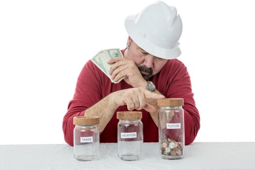 Construction worker wearing a hardhat deciding over the use of money between, taxes, vacations or tuitions