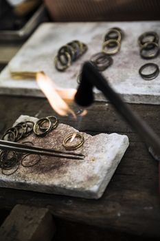 Jeweler crafting golden rings with flame torch.