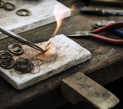 Close up of Jeweler crafting golden rings with flame torch.