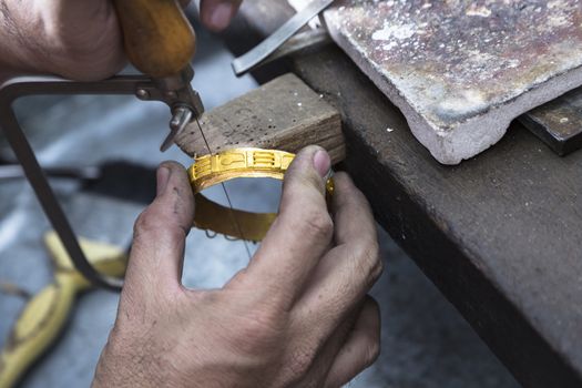 Close up of Jeweler crafting golden bangle with flame torch.