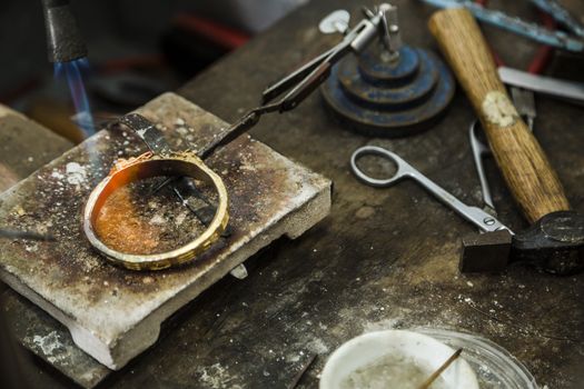 Close up of Jeweler crafting golden rings with flame torch.