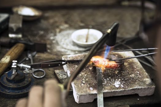 Close up of Jeweler crafting golden rings with flame torch.