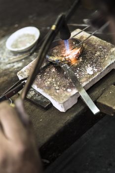 Vertical close up shot of Jeweler crafting golden rings with flame torch.