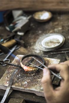 Vertical close up shot of Jeweler crafting golden rings with flame torch.