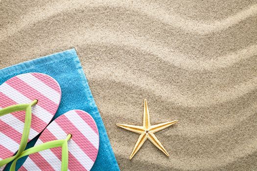 Sand background with towel, flip flops and starfish. Summer concept. Top view
