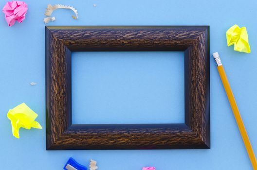empty wooden picture frame on a blue background with writing equipment and sharpening shavings