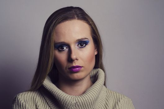 fashion portrait of a blonde woman in studio wearing a heavy make up and a turtleneck sweater