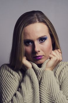 fashion portrait of a blonde woman in studio wearing a heavy make up and a turtleneck sweater vertically cropped