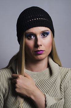 fashion portrait of a blonde woman in studio wearing a heavy make up and a turtleneck sweater with a black knitted hat vertically cropped