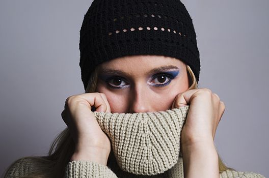 blonde woman wearing a black knitted hat covering her face with turtleneck sweater