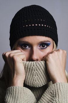 blonde woman wearing a black knitted hat covering her face with turtleneck sweater vertically cropped