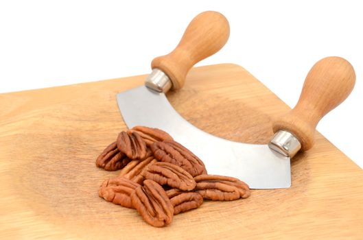 Whole pecan nuts with a rocking knife on a wooden chopping board