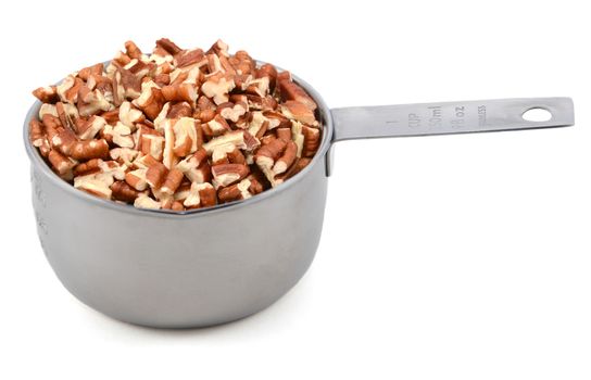 Chopped pecan nuts in a metal cup measure, isolated on a white background