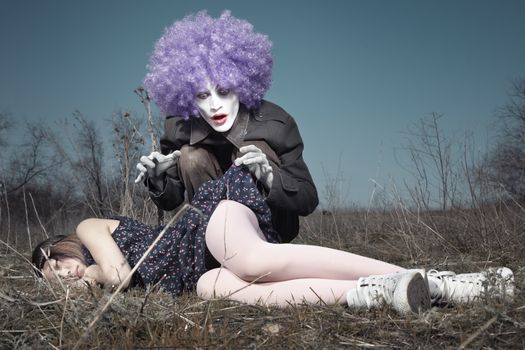 Sleeping girl outdoors and crazy maniac clown touching her shirt. Artistic colors added