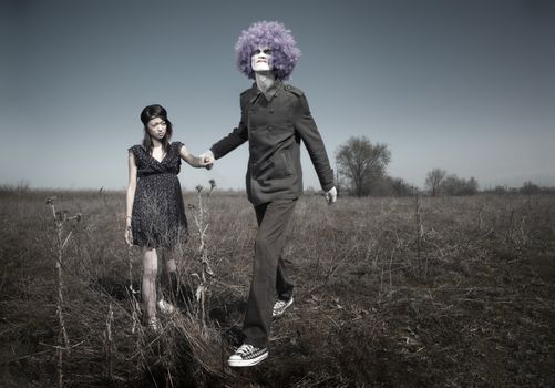 Bizarre couple in relationship conflict. Crazy clown and little girl outdoors. Natural lights and colors