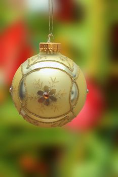 gold christmas ball hanging from the tree over colorful out of focus background