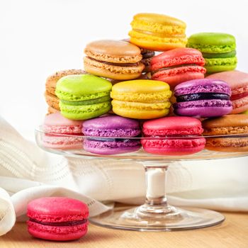 traditional french colorful macarons in a glass cake stand on wooden table