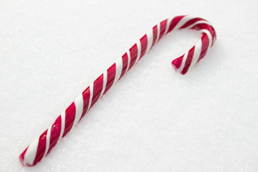 Sweet red and white candy cane lying in the snow.