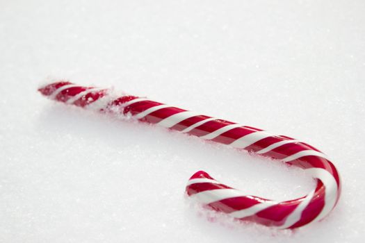 Sweet red and white candy cane lying in the snow.