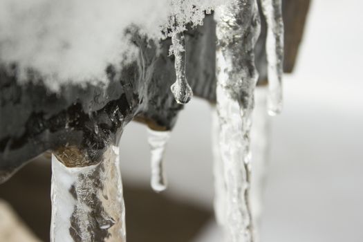 Icicles on a outdoor bench covered with snow and ice.